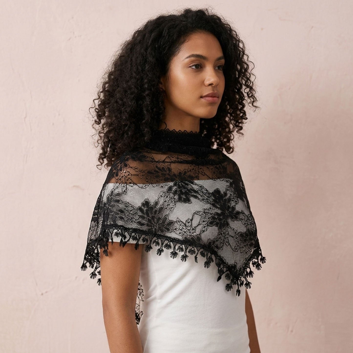 Woman with curly hair wearing black lace triangle scarf on pink background