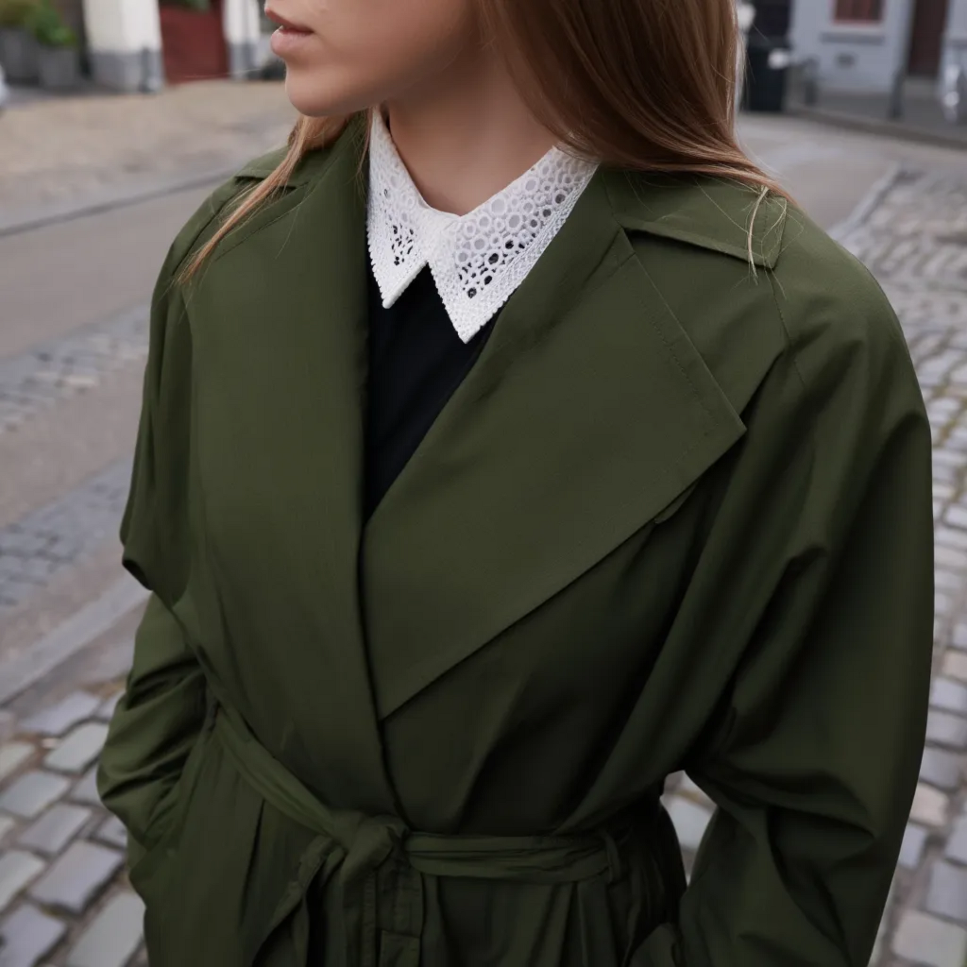 Woman wearing white lace collar with dark green coat on city street