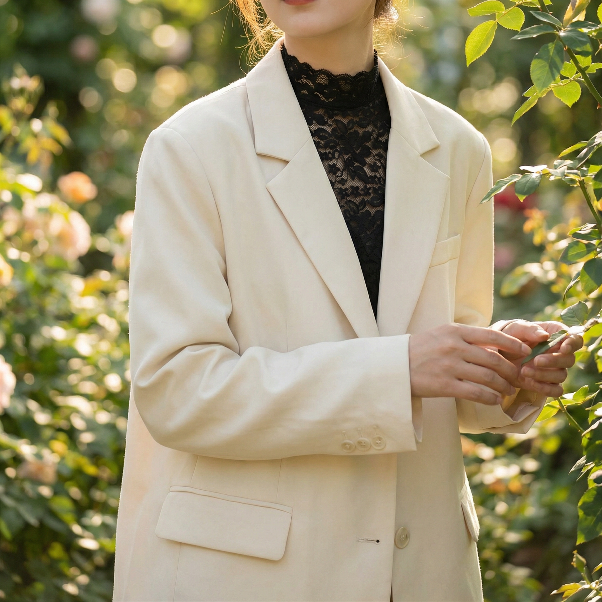 Woman wearing white lace crop top with cream blazer, hands clasped