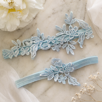 Sky blue lace bridal garter set flat lay on floral background
