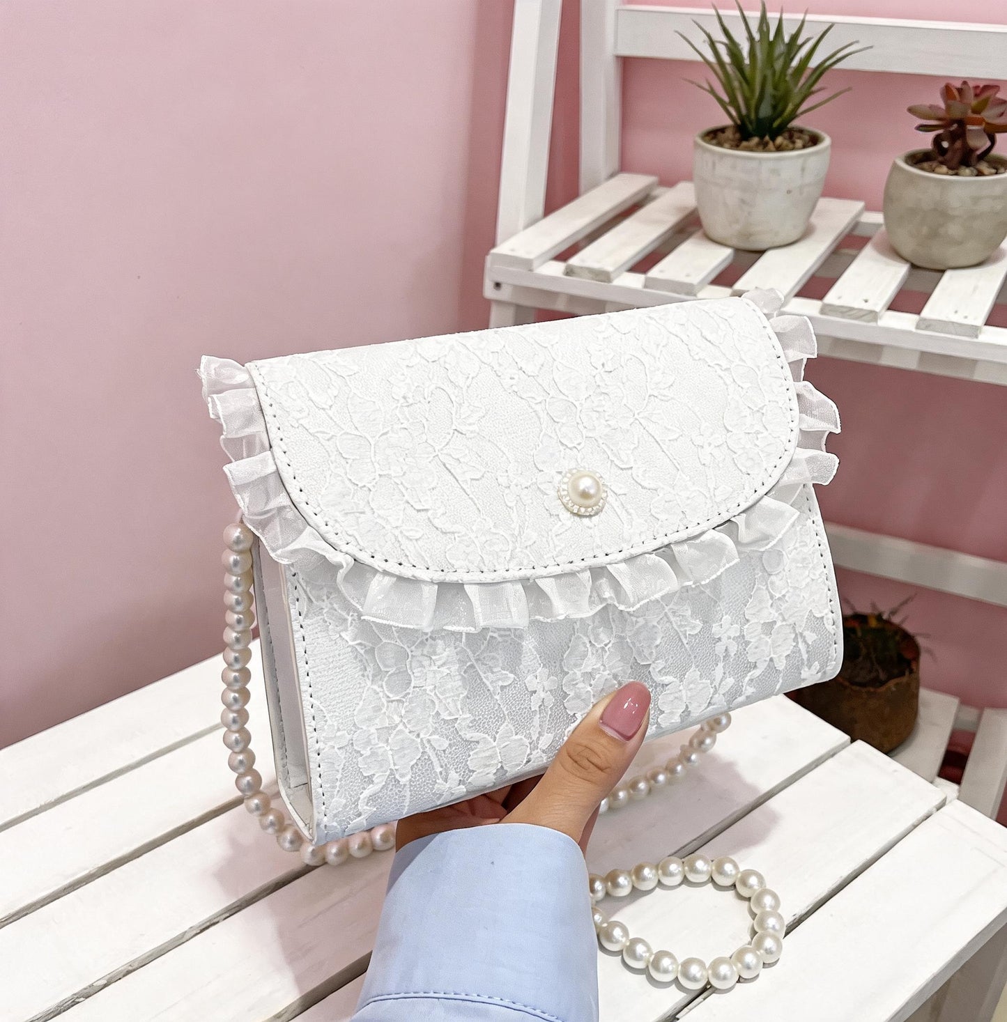 Hand holding white lace crossbody bag on white surface