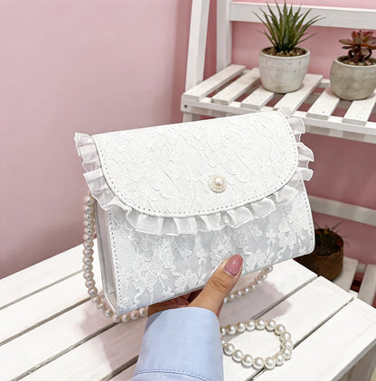 Hand holding white lace crossbody bag on white surface