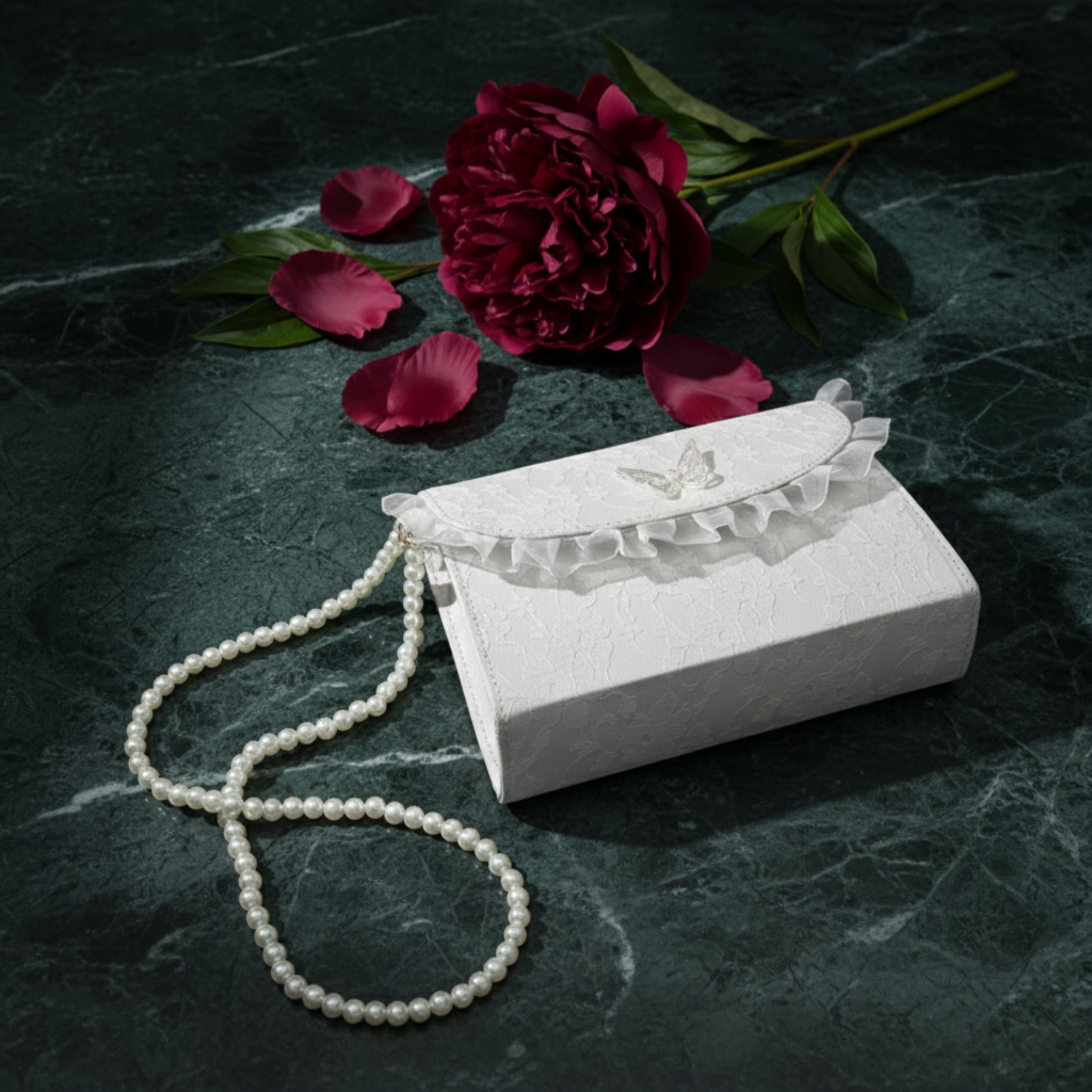 White lace crossbody bag with pearl chain on dark green marble with red roses