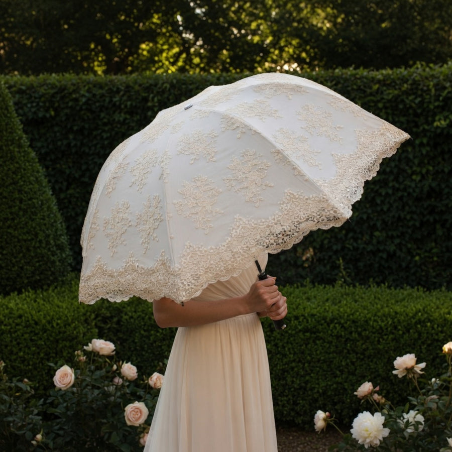 Woman holding white lace embroidery umbrella by hedge