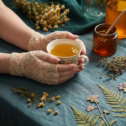 Beige lace fingerless gloves holding a cup of tea, floral lace detail