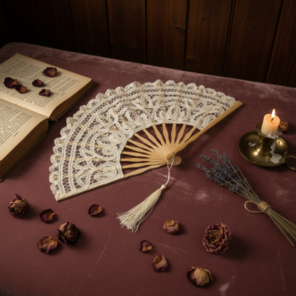 White lace hand fan on burgundy surface with candle