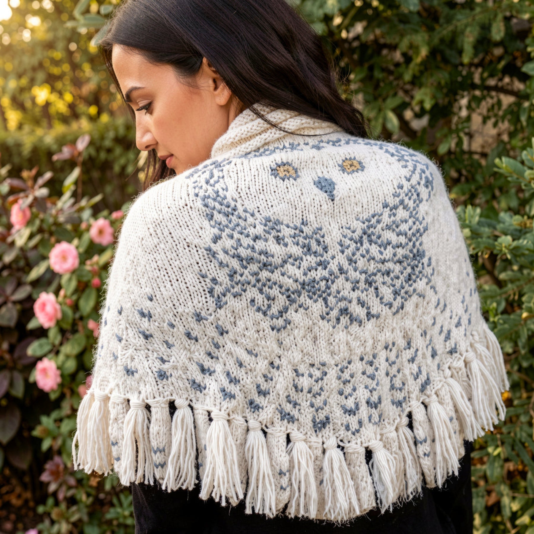 Woman wearing snowy owl wings shawl in garden with pink flowers