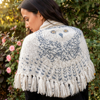 Woman wearing snowy owl wings shawl in garden with pink flowers