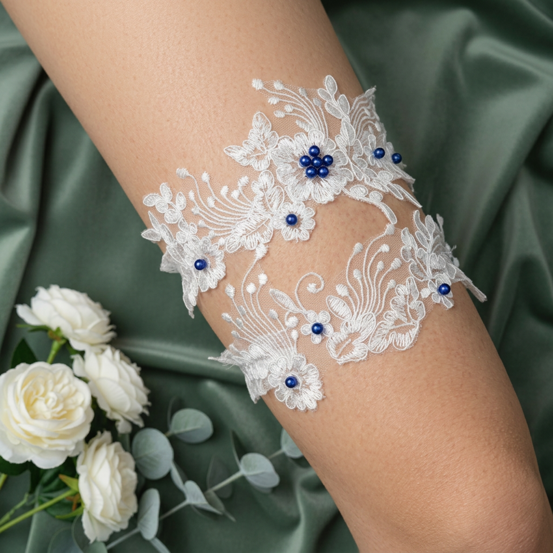 Lace wedding garter with pearl beads on arm with green fabric and roses